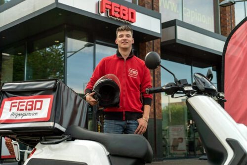 FEBO-bezorger poseert met helm naast zijn scooter voor een FEBO-winkel