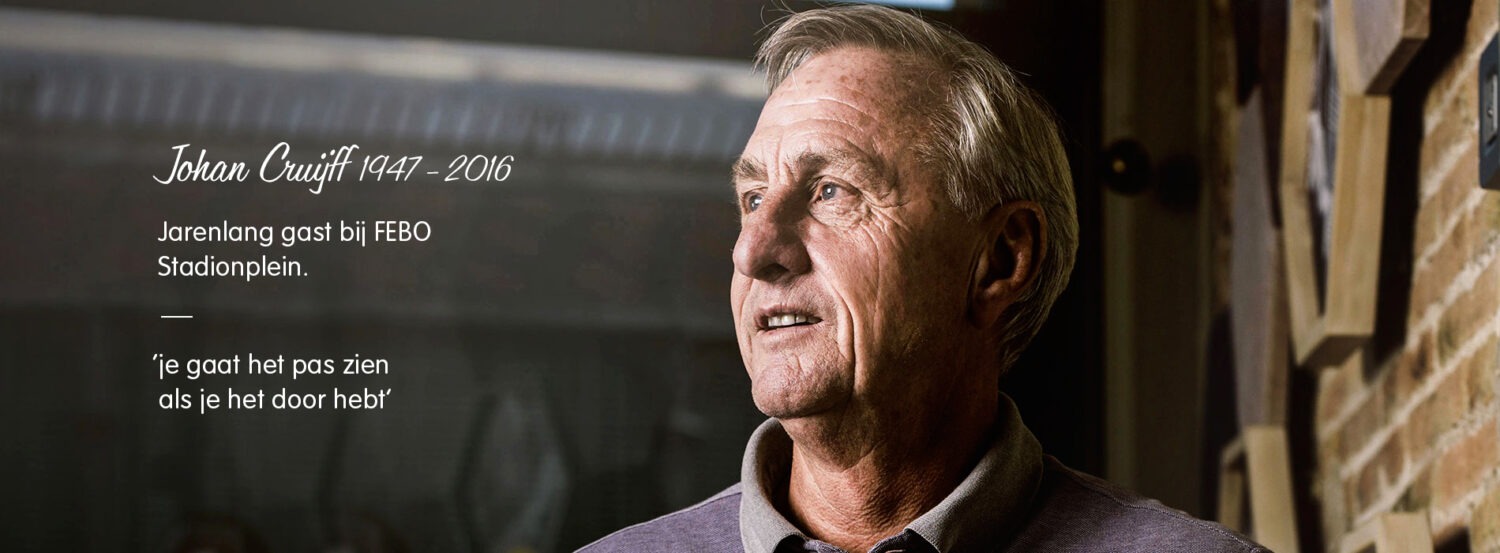 Johan Cruijff poseert voor de camera bij FEBO Stadionplein, met tekst 'Je gaat het pas zien als je het door hebt'