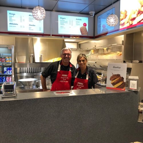 Twee FEBO-medewerkers staan lachend naast elkaar achter de toonbank